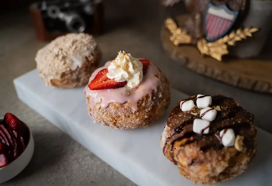 Three layered doughnuts on a marble board: cinnamon crumb, strawberry with whipped cream, and s'mores