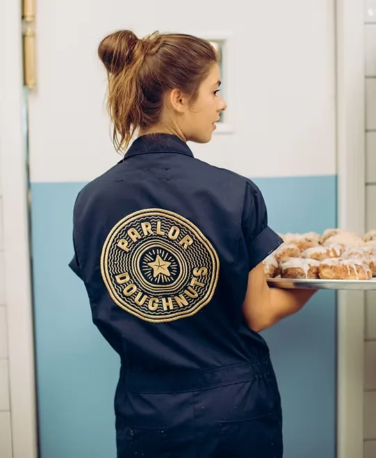 Parlor team member in a navy jacket with the Parlor seal, carrying a tray of doughnuts